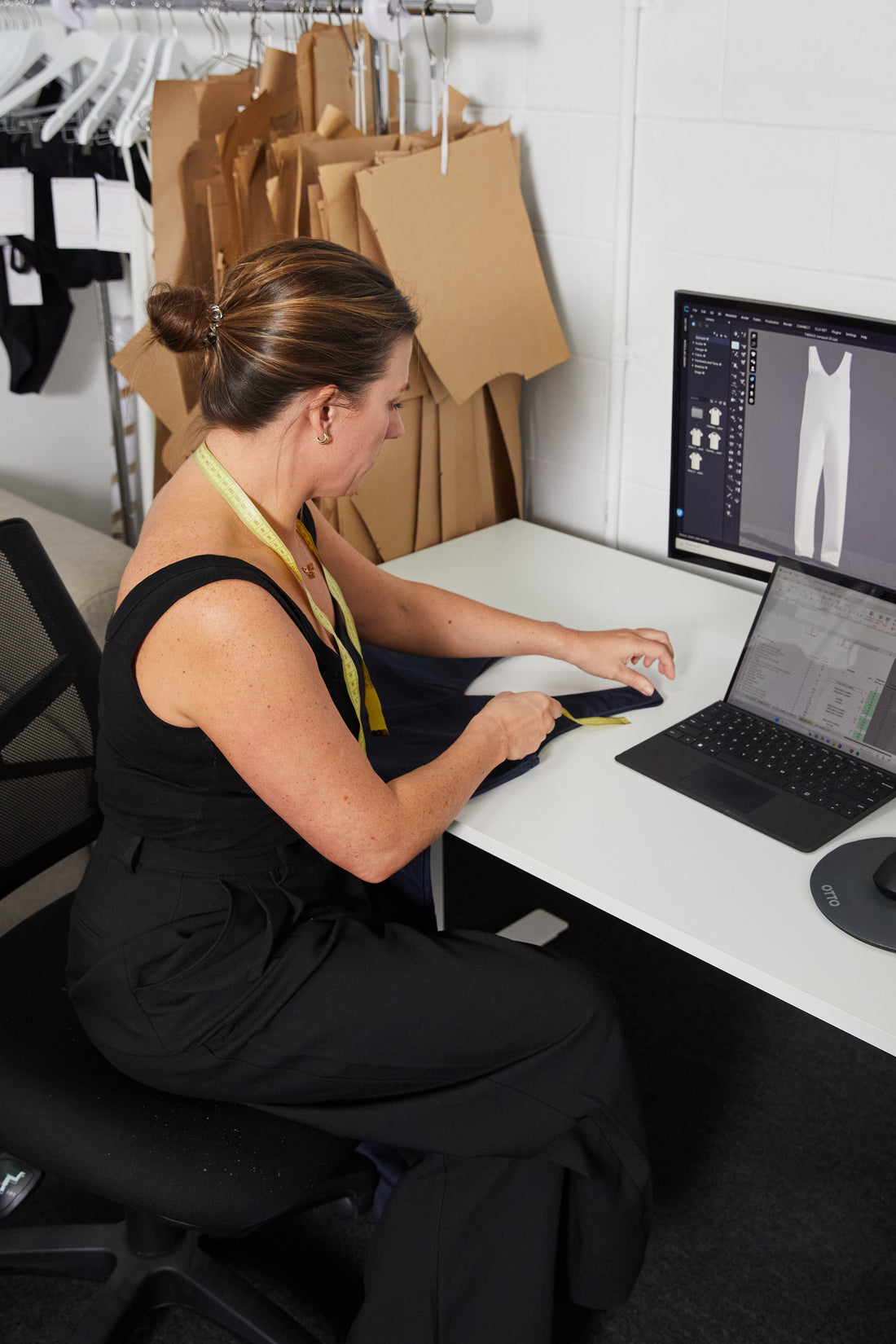 woman working in a fashion studio using CLO3d pattern making system with a tape measure  and paper patterns