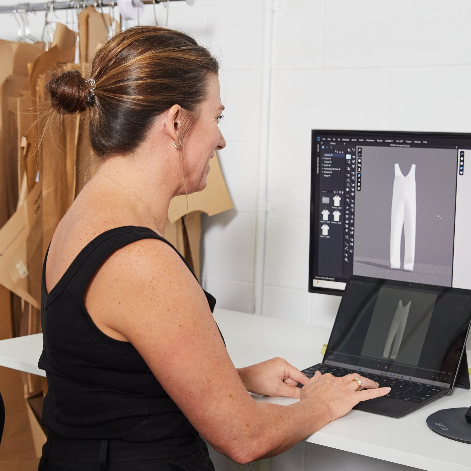 Person using a laptop with CLO3D design software on a desk in an office setting.